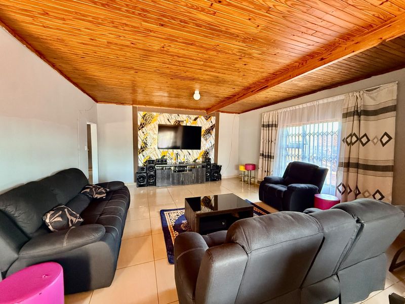 Spacious living room featuring a warm timber-clad ceiling, large tiled flooring, and a decorative feature wall with integrated television mounting.