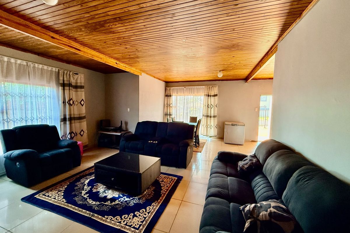 Spacious living area featuring a warm timber tongue and groove ceiling, neutral tiled flooring, and natural light through sliding glass doors.