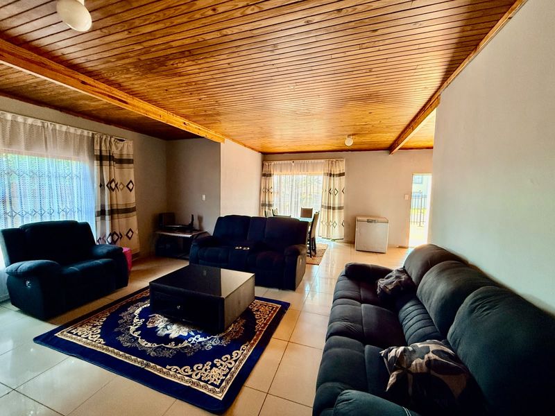 Spacious living area featuring a warm timber tongue and groove ceiling, neutral tiled flooring, and natural light through sliding glass doors.