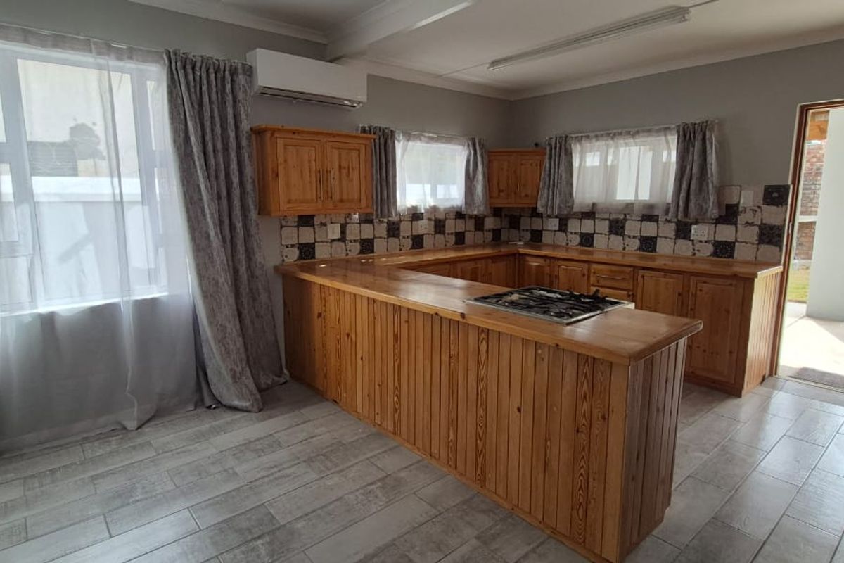 A functional kitchen featuring wooden cabinetry, a gas hob, tiled backsplash, and direct access to an outdoor area.