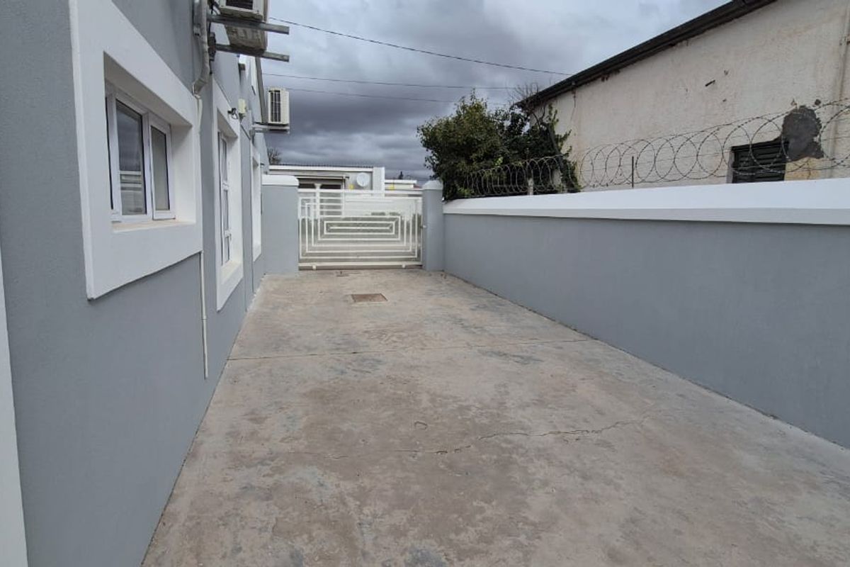 A paved side or rear access area featuring a perimeter wall with security razor wire and a metal gate.