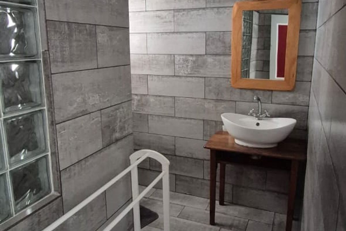 A modern bathroom featuring grey ceramic wall and floor tiles, a vessel sink, and a distinctive glass block wall section.