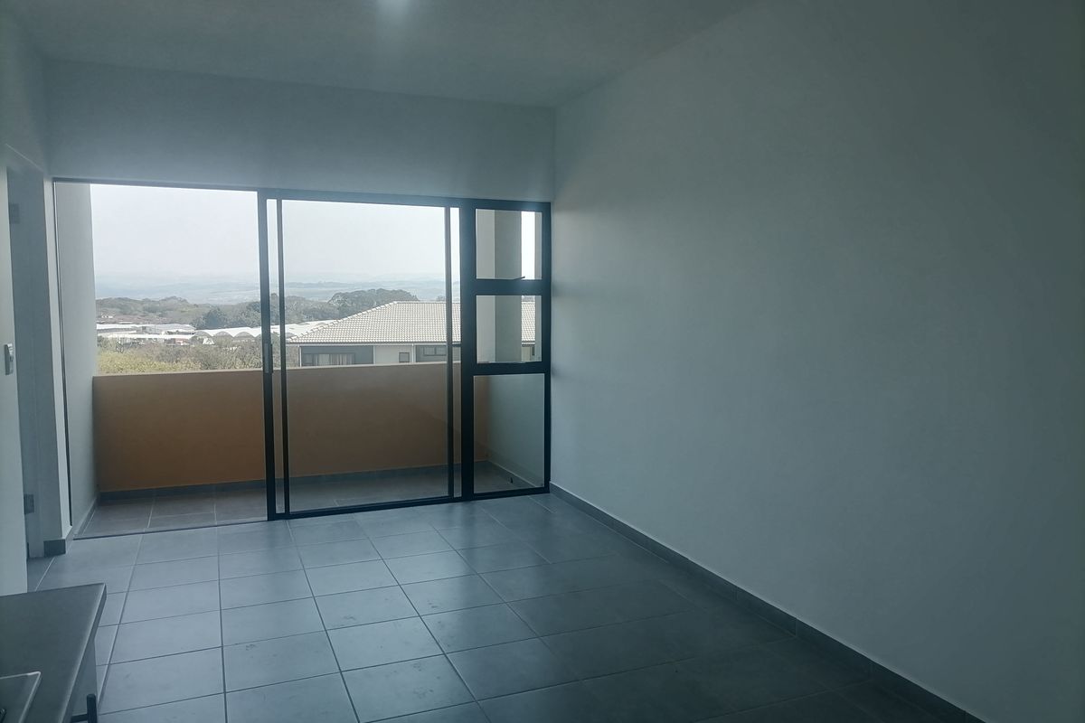 An empty open-plan living area featuring neutral tiled flooring, recessed lighting, and large sliding glass doors leading to a private balcony with scenic views.