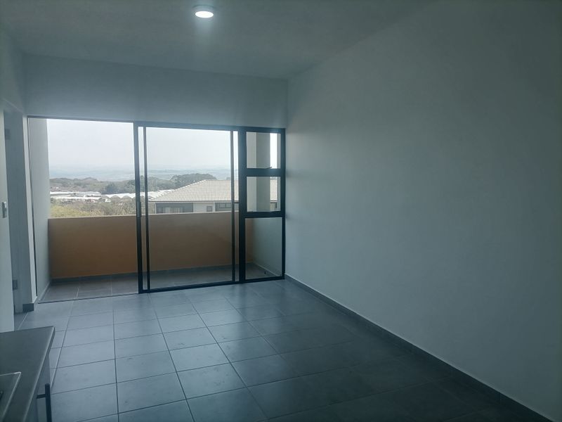 An empty open-plan living area featuring neutral tiled flooring, recessed lighting, and large sliding glass doors leading to a private balcony with scenic views.