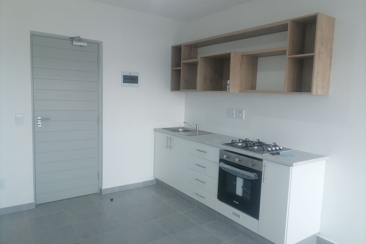 A clean, modern kitchen featuring white cabinetry, built-in oven, gas hob, and open shelving, set against neutral tiled floors and walls.