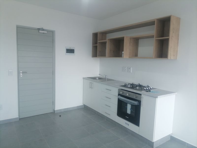 A clean, modern kitchen featuring white cabinetry, built-in oven, gas hob, and open shelving, set against neutral tiled floors and walls.