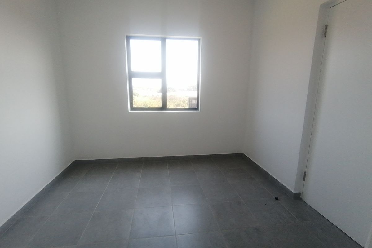 A clean, empty bedroom featuring neutral tiled flooring, white walls, and an aluminium-framed window providing natural light.