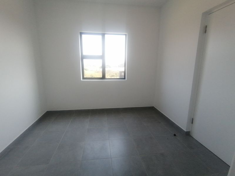 A clean, empty bedroom featuring neutral tiled flooring, white walls, and an aluminium-framed window providing natural light.