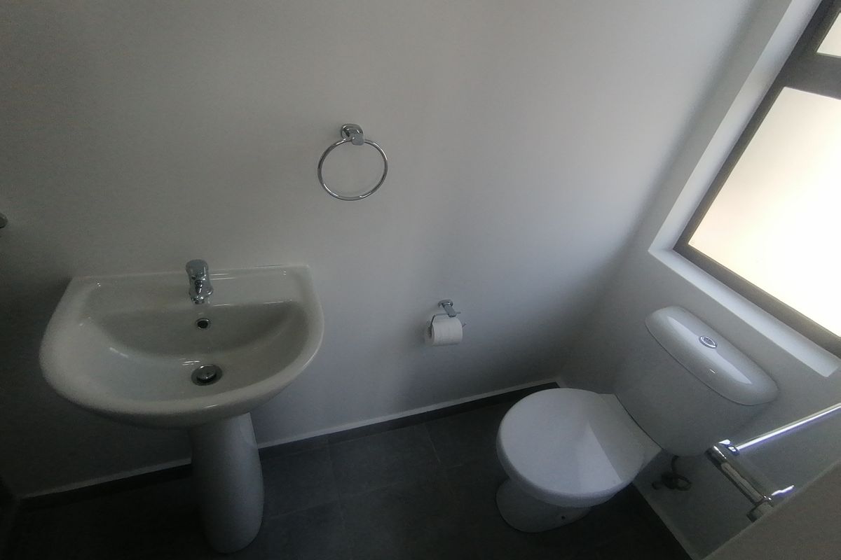 A clean and functional bathroom featuring a pedestal basin, toilet, and tiled flooring with neutral finishes.