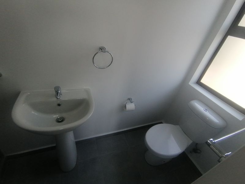 A clean and functional bathroom featuring a pedestal basin, toilet, and tiled flooring with neutral finishes.