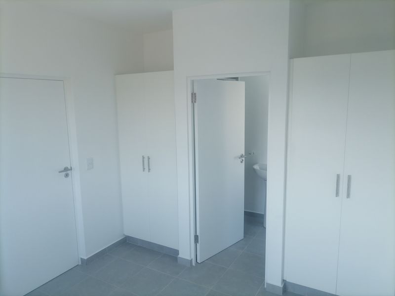 A clean, empty bedroom featuring neutral tiled flooring, white built-in cupboards, and direct access to an en-suite bathroom.