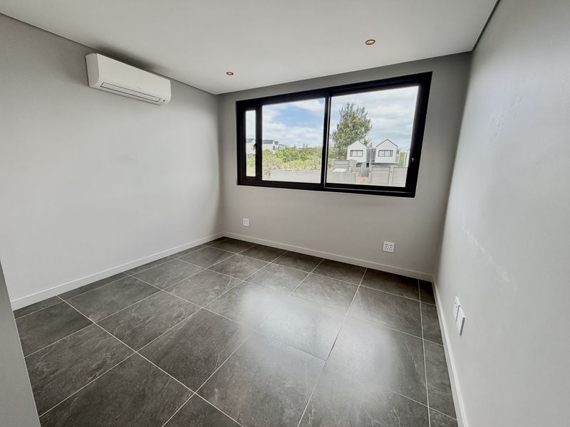 A bright, empty bedroom featuring modern dark floor tiles, recessed lighting, and a wall-mounted air conditioning unit.