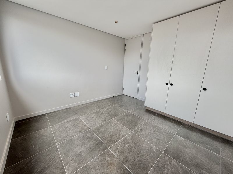 A clean, modern bedroom featuring neutral walls, large-format grey floor tiles, and built-in storage cupboards.