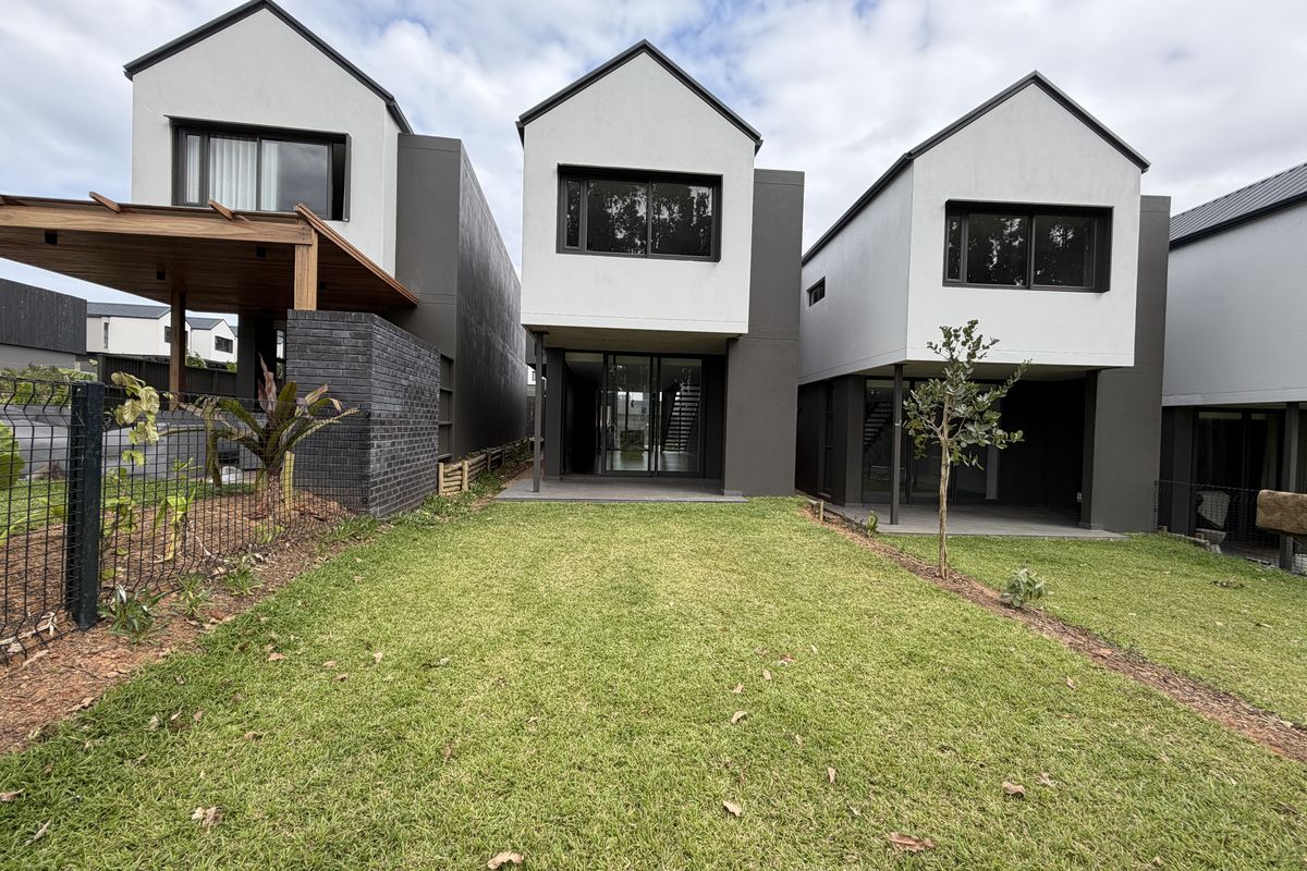 Rear view of modern townhouse development featuring a private lawn, timber pergola, and contemporary architectural design with sliding glass doors.