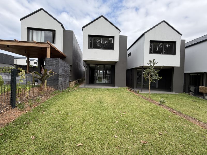 Rear view of modern townhouse development featuring a private lawn, timber pergola, and contemporary architectural design with sliding glass doors.