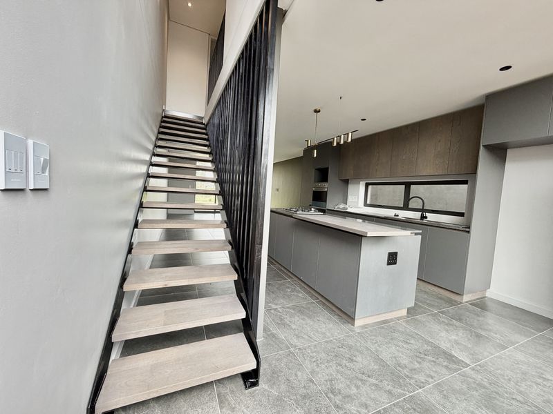 Modern open-plan kitchen featuring a central island, sleek cabinetry, and integrated appliances, adjacent to a contemporary staircase with a metal balustrade.