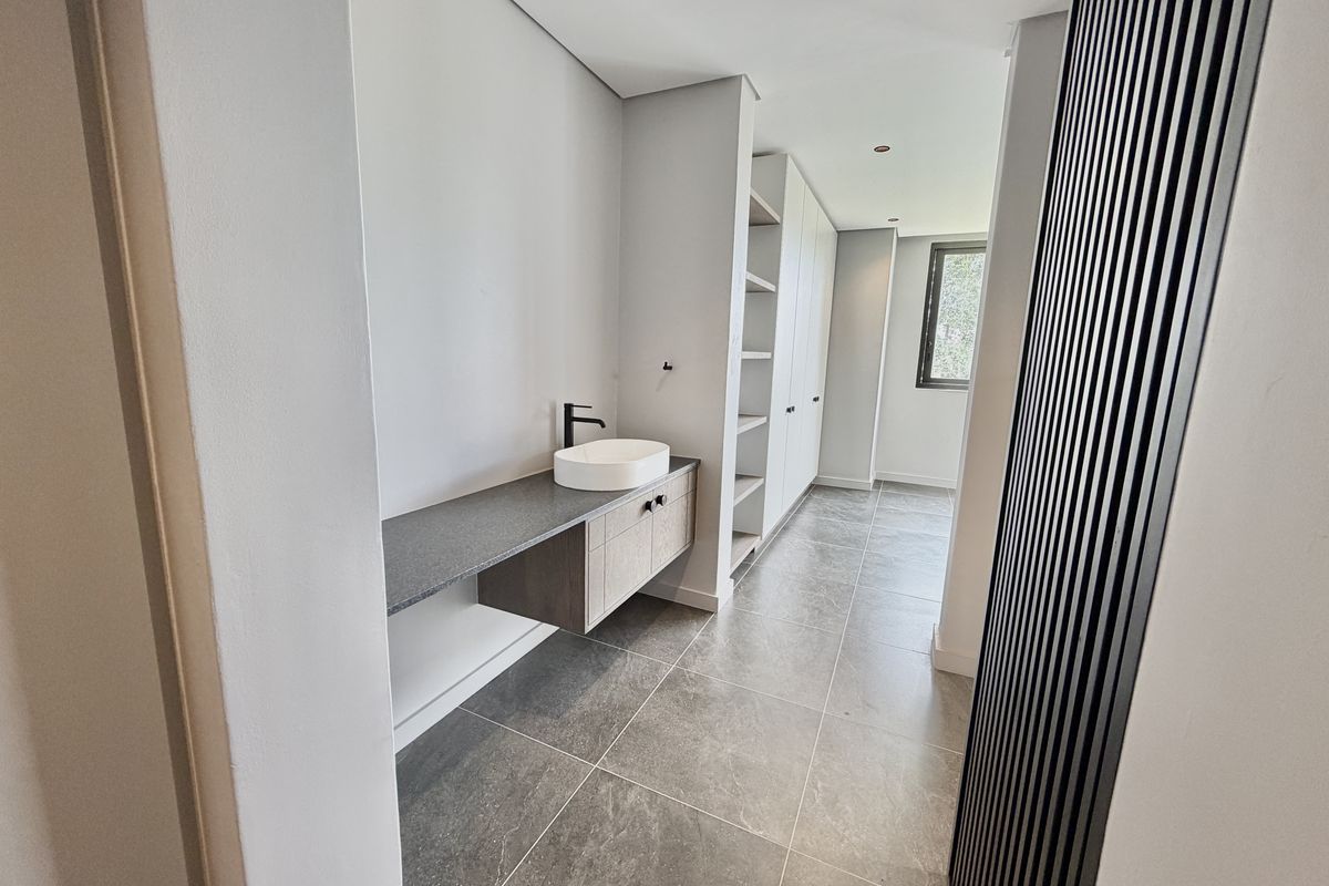Modern bathroom featuring a floating vanity with a vessel sink, black fixtures, built-in shelving, and contemporary tiled flooring.