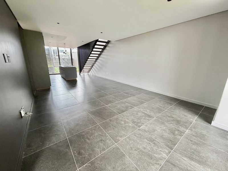 Spacious open-plan living area featuring modern tiled flooring, a sleek staircase, and a central kitchen island in a contemporary townhouse setting.