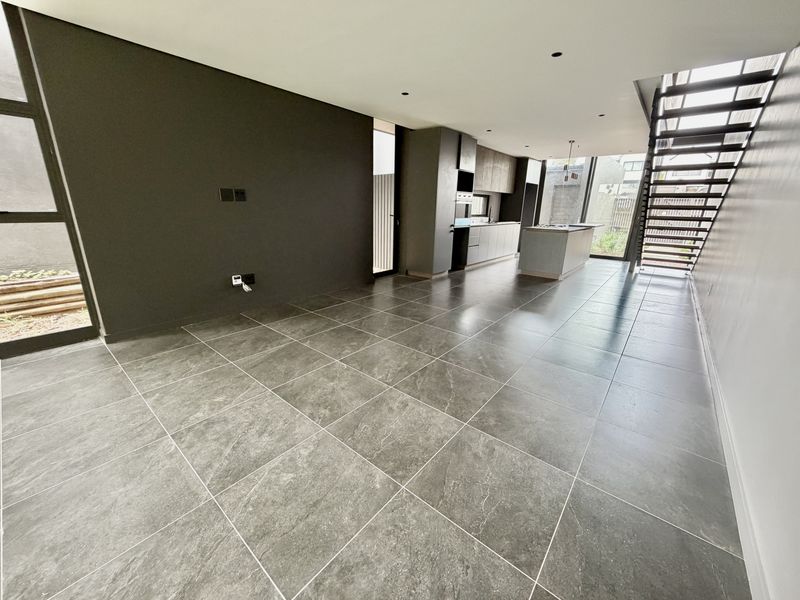 Spacious open-plan living and kitchen area featuring modern tiled floors, sleek cabinetry, a central island, and a contemporary staircase leading to the upper level.