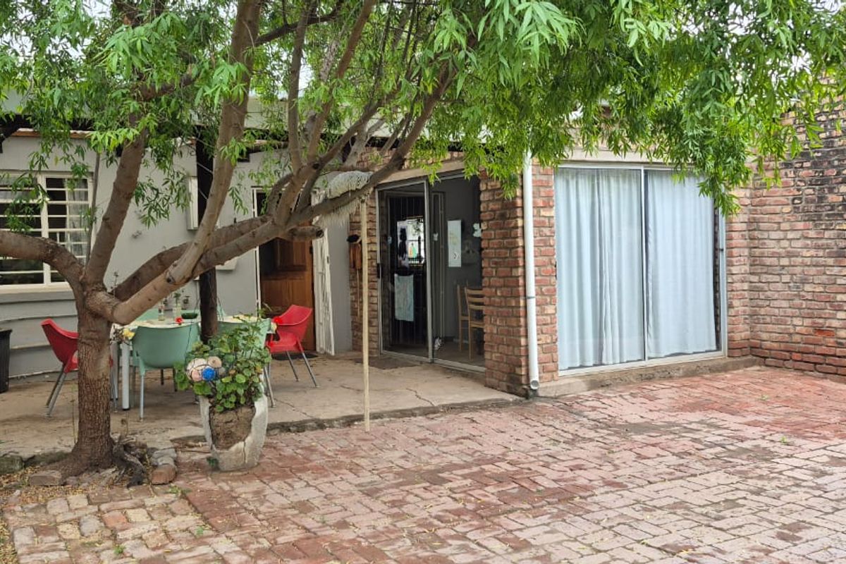 Rear exterior view of the house featuring a brick chimney, paved patio area, and sliding glass door access to the interior.