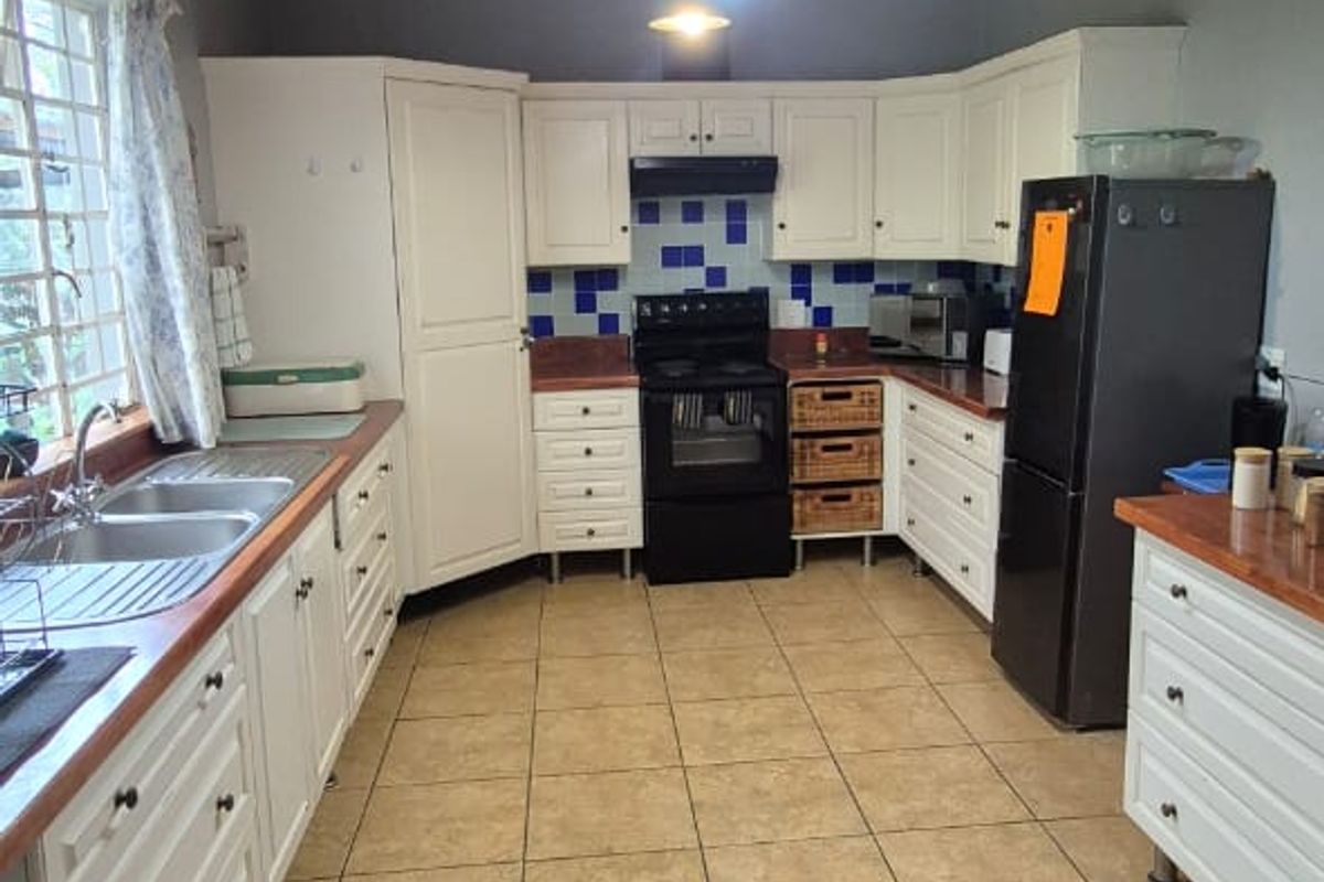 A functional kitchen featuring white cabinetry, timber countertops, tiled flooring, and an exposed ceiling beam, offering a classic layout with ample storage space.