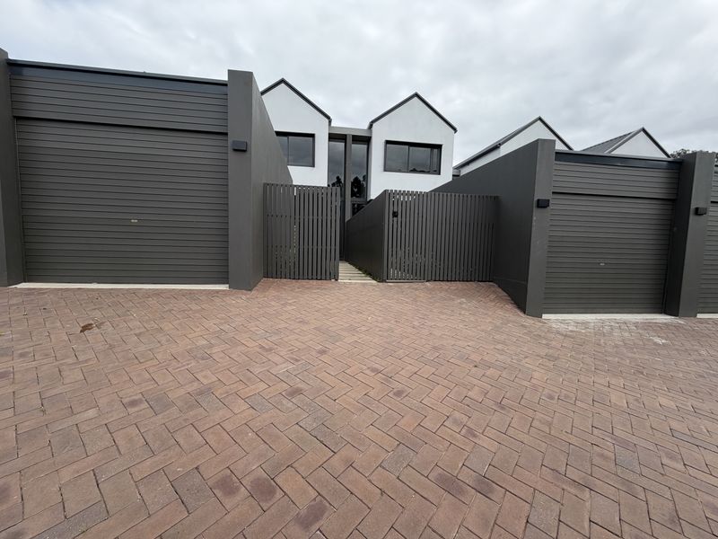 Modern townhouse exterior featuring a paved driveway, double garage access, and contemporary gabled architecture with timber slat privacy fencing.