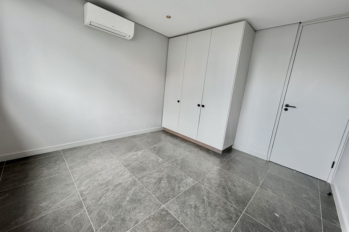 A clean, modern bedroom featuring large-format grey floor tiles, a built-in wardrobe, and a wall-mounted air conditioning unit.