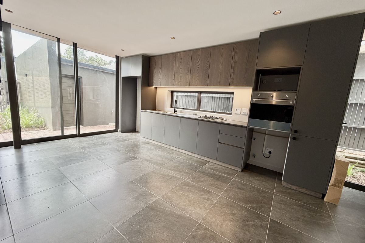 Modern kitchen featuring sleek dark cabinetry, integrated appliances, stone countertops, and large format floor tiles with direct access to an outdoor patio area.