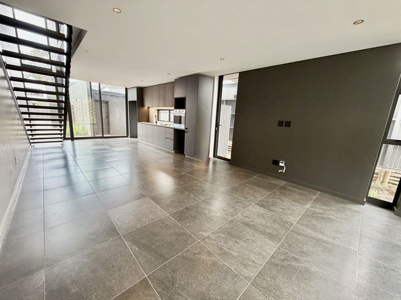 Spacious open-plan living area featuring modern kitchen cabinetry, integrated oven, sleek tiled flooring, and a contemporary staircase leading to the upper level.