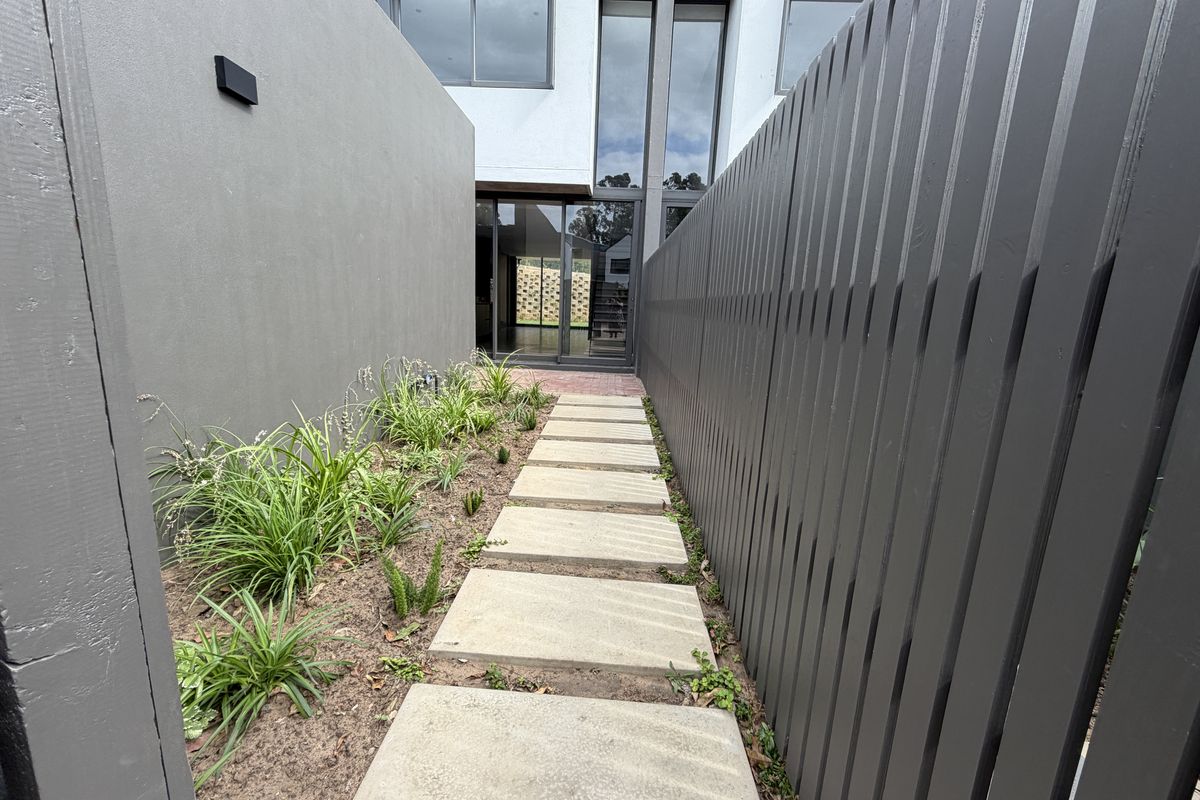 A modern side pathway featuring concrete pavers, landscaped garden beds, and contemporary timber slat fencing leading to the rear entrance of the townhouse.