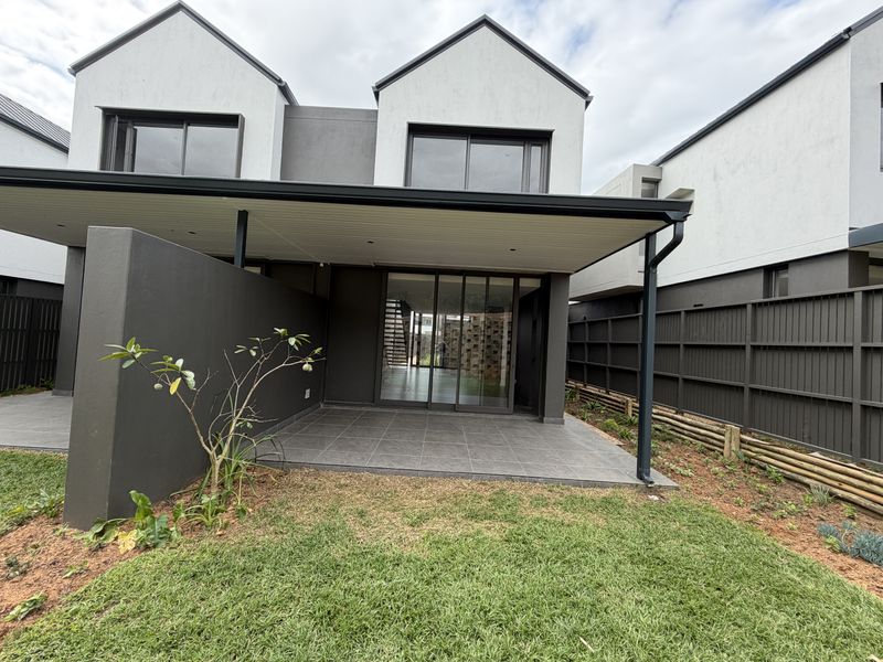 A modern townhouse rear elevation featuring a covered tiled patio, sliding glass doors, and a private garden area with perimeter fencing.