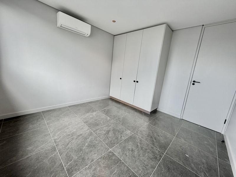 A clean, modern bedroom featuring large-format grey floor tiles, a built-in wardrobe, and a wall-mounted air conditioning unit.