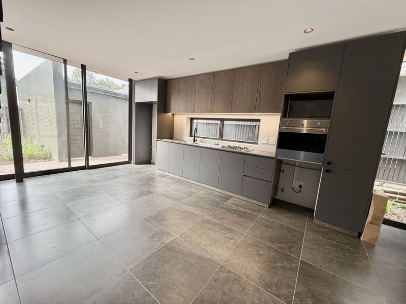 Modern kitchen featuring sleek dark cabinetry, integrated appliances, stone countertops, and large format floor tiles with direct access to an outdoor patio area.