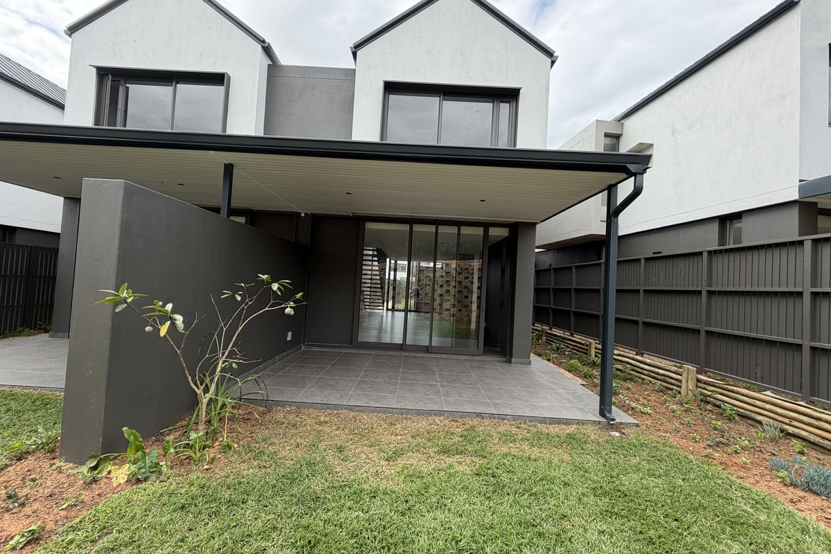 A modern townhouse rear elevation featuring a covered tiled patio, sliding glass doors, and a private garden area with perimeter fencing.