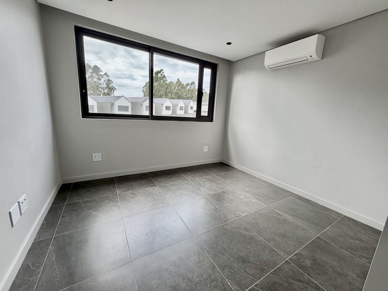A bright, empty bedroom featuring modern grey floor tiles, a large sliding window, and a wall-mounted air conditioning unit.