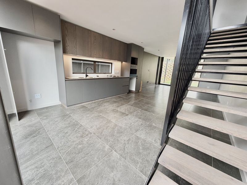 Modern open-plan kitchen featuring sleek cabinetry, integrated appliances, and large format floor tiles, adjacent to a contemporary staircase with a metal balustrade.