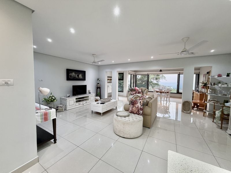 Spacious open-plan living and dining area featuring polished porcelain floor tiles, recessed lighting, ceiling fans, and large glass doors leading to a scenic view.