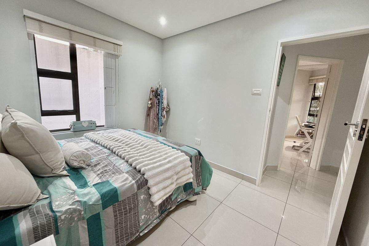 A well-maintained bedroom featuring neutral tiled flooring, recessed lighting, and an aluminium-framed window with a roller blind.