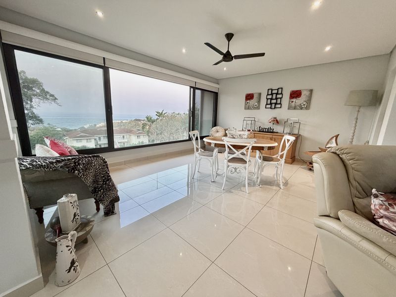 Spacious open-plan living and dining area featuring large sliding glass doors with ocean views, recessed lighting, and polished porcelain floor tiles.