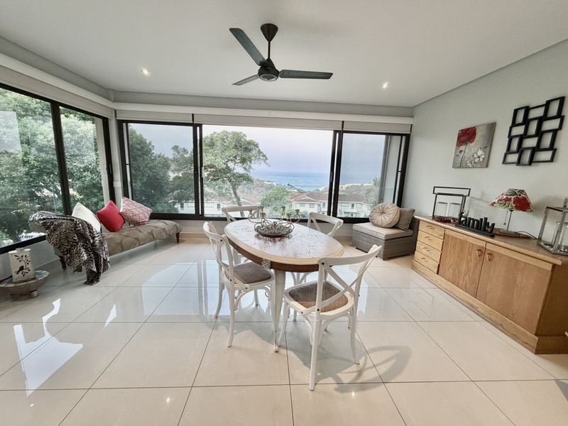 Bright dining area featuring large format floor tiles, recessed lighting, and expansive sliding glass doors offering scenic coastal views.
