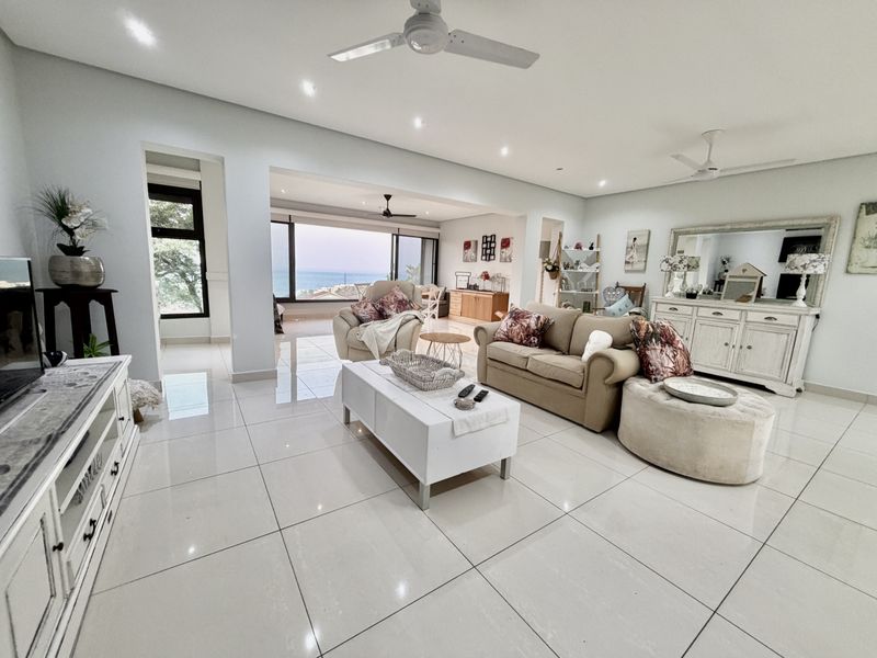 Spacious open-plan living area featuring polished tiled floors, recessed lighting, ceiling fans, and large windows with scenic ocean views.