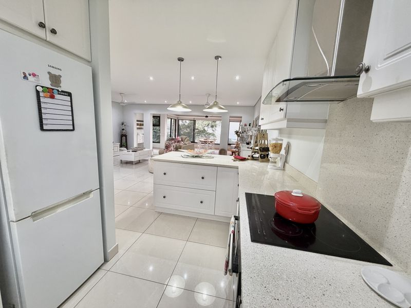 Spacious open-plan kitchen and living area featuring modern shaker-style cabinetry, stone countertops, an electric cooktop, and sleek tiled flooring throughout.