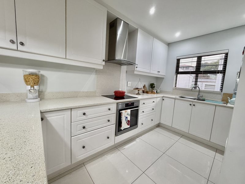 Modern kitchen featuring white cabinetry, stone countertops, stainless steel appliances, and tiled flooring, offering a clean and functional workspace.
