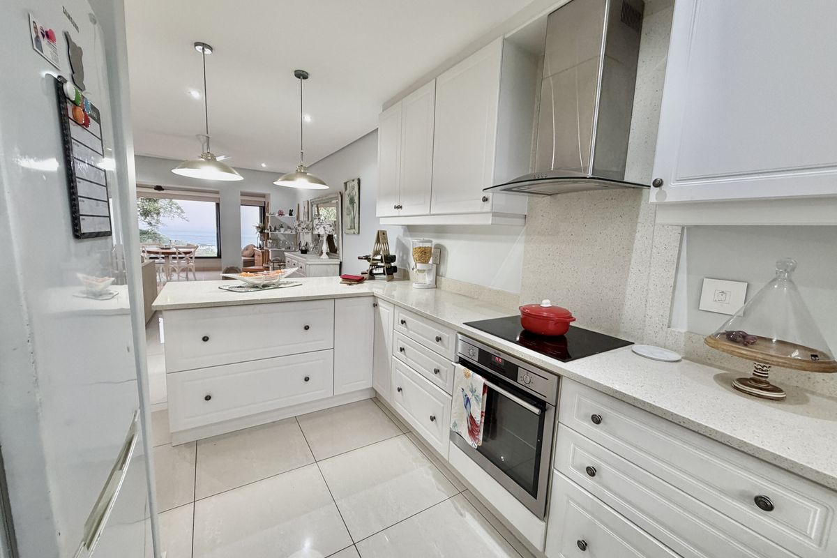 Modern open-plan kitchen featuring white shaker-style cabinetry, stone countertops, integrated appliances, and tiled flooring, flowing seamlessly into the adjacent living and dining area.