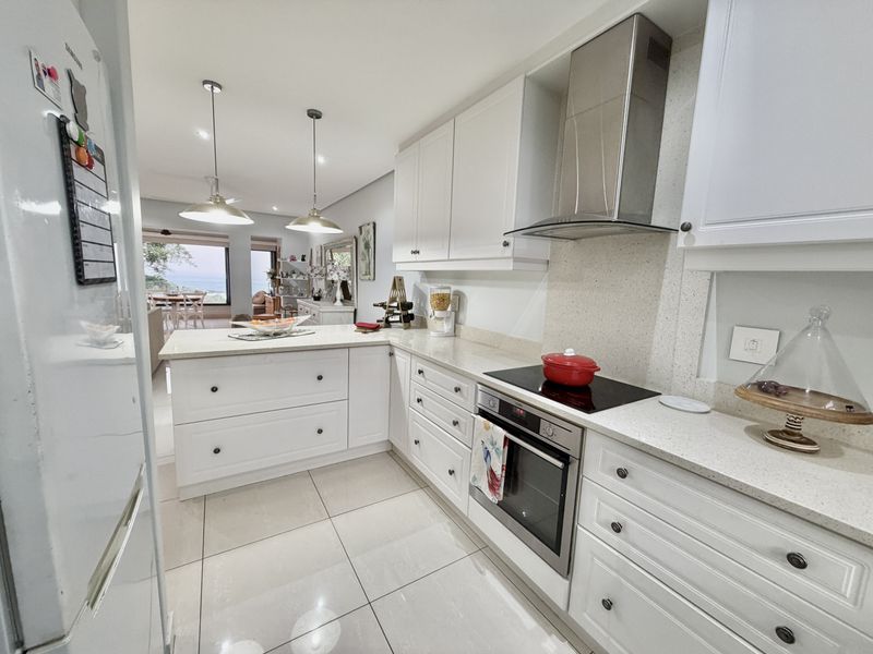 Modern open-plan kitchen featuring white shaker-style cabinetry, stone countertops, integrated appliances, and tiled flooring, flowing seamlessly into the adjacent living and dining area.