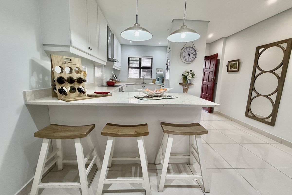 Modern kitchen featuring white cabinetry, quartz countertops, a breakfast bar, and sleek ceramic floor tiles, creating a bright and functional culinary space.