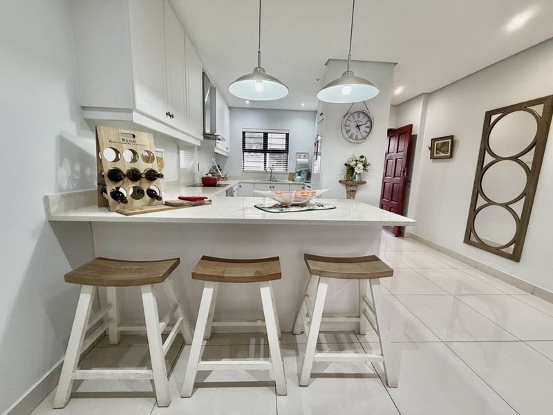 Modern kitchen featuring white cabinetry, quartz countertops, a breakfast bar, and sleek ceramic floor tiles, creating a bright and functional culinary space.