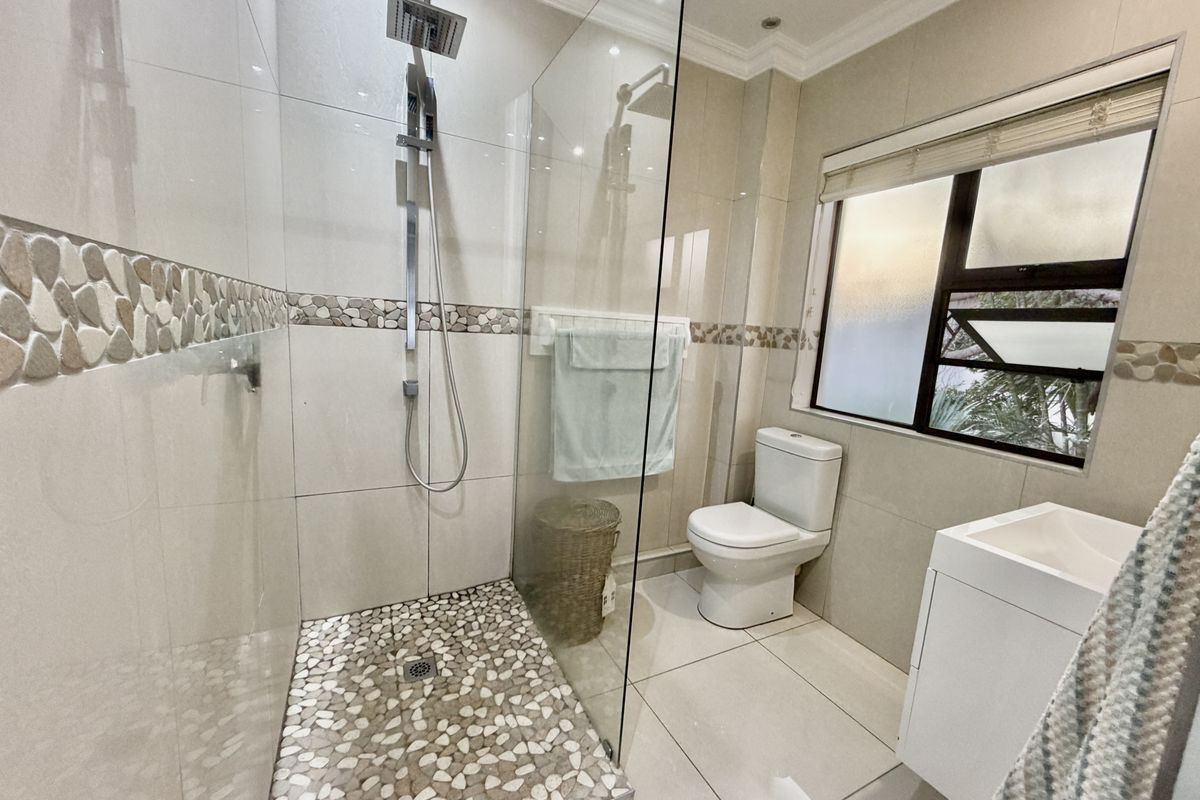 Modern bathroom featuring a walk-in shower with a rainfall shower head, pebble tile flooring, glass screen, toilet, and a vanity cabinet.