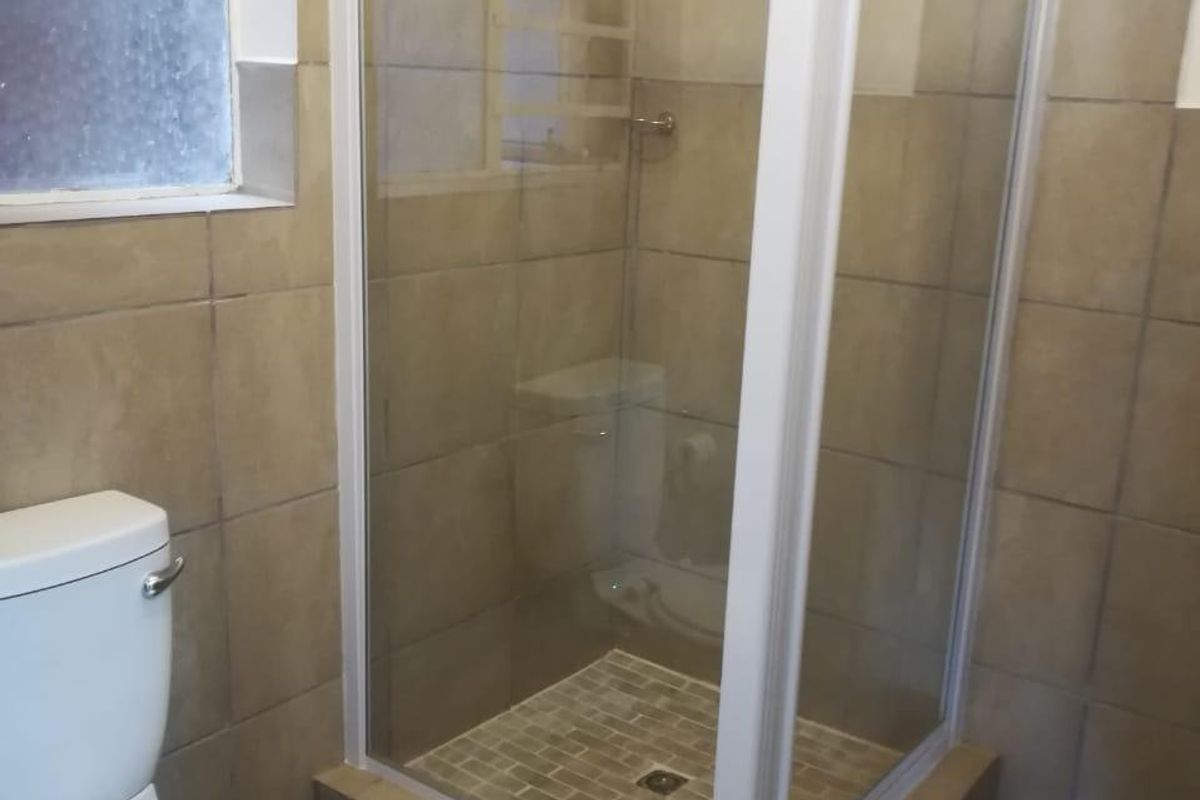 A functional bathroom featuring a corner shower enclosure, a standard toilet, and neutral wall and floor tiling.