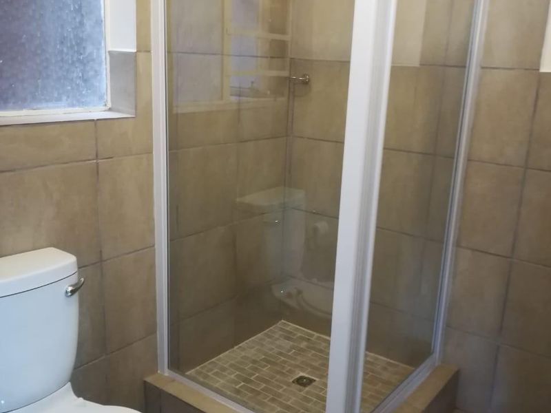 A functional bathroom featuring a corner shower enclosure, a standard toilet, and neutral wall and floor tiling.